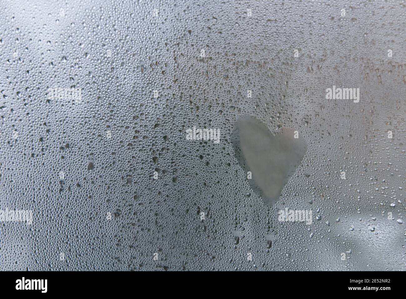 Selektiver Fokus und Makroansicht bei der Handschrift von Herzmustern und Tropfen Wasser, Tau oder Strom auf Glas Fenster. Stockfoto