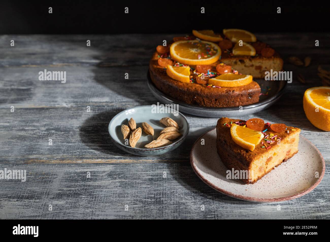 Orangefarbener Kuchen auf grauem Holzhintergrund. Hartes Licht. Kontrast, Low-Key. Seitenansicht, Kopierbereich. Stockfoto