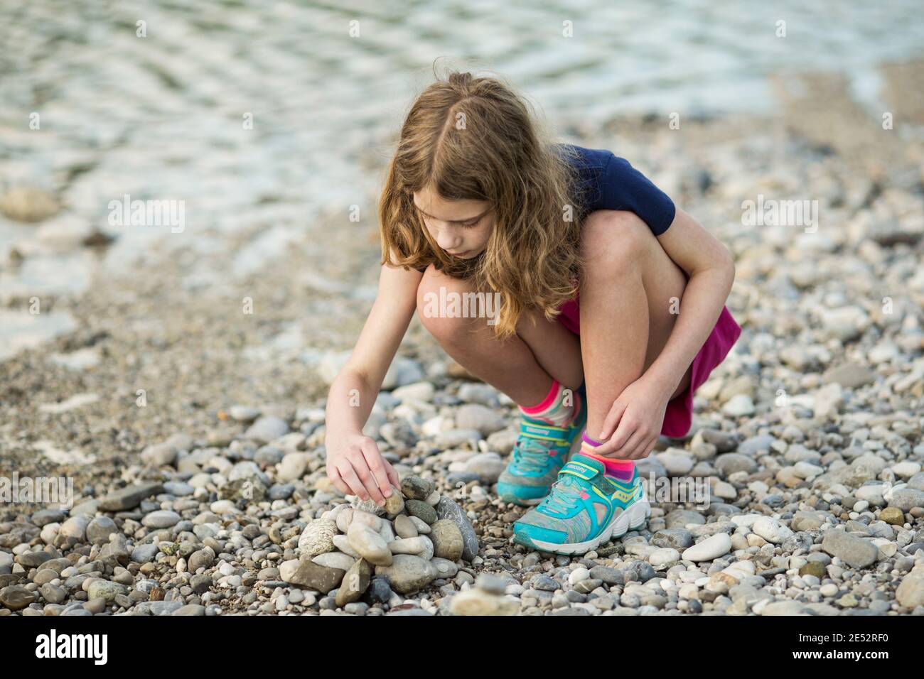 Ein elfjähriges Mädchen stapelt am Ufer der Isar in München Steine in eine Kaira. Stockfoto