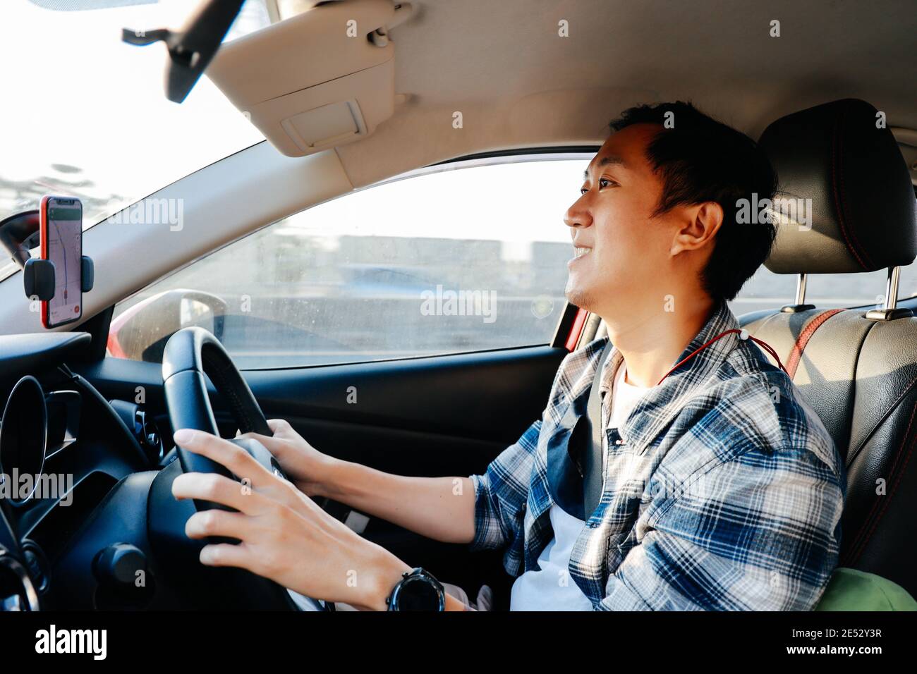 Nahaufnahme des jungen asiatischen Mannes lächelnd und Blick auf die Stadtstraße während der Fahrt mit dem Auto in der Stadt Stockfoto