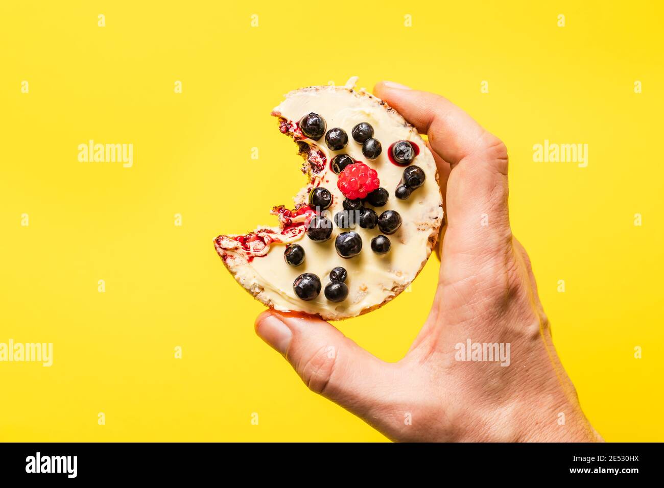 Hand halten knusprig aufgeblasen Reiskuchen mit frischen Früchten Blaubeeren Himbeeren vor dem gelben Hintergrund - gesund Bio-Vegetarier oder ve Stockfoto