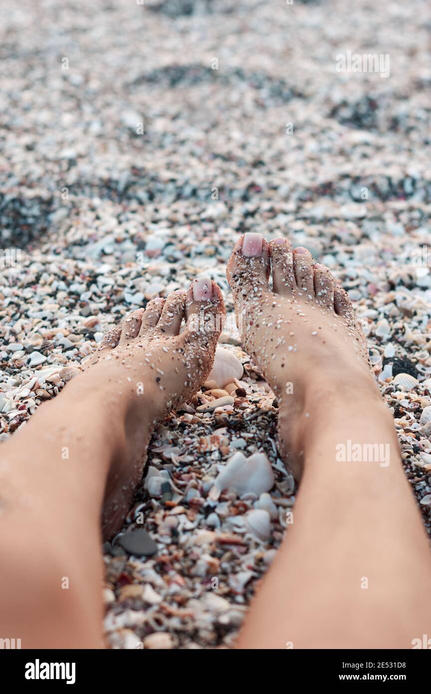 Die Füße einer Frau liegen an einem Strand voller Muscheln Stockfoto