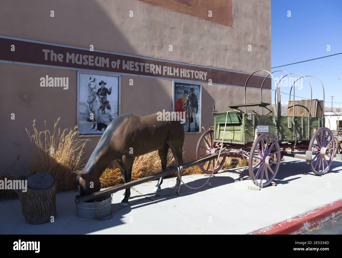 Vintage Western Wagon Wheel Replik vor dem Museum of Western Film History in Lone Pine, Kalifornien mit alten Filmplakaten an der Außenwand Stockfoto