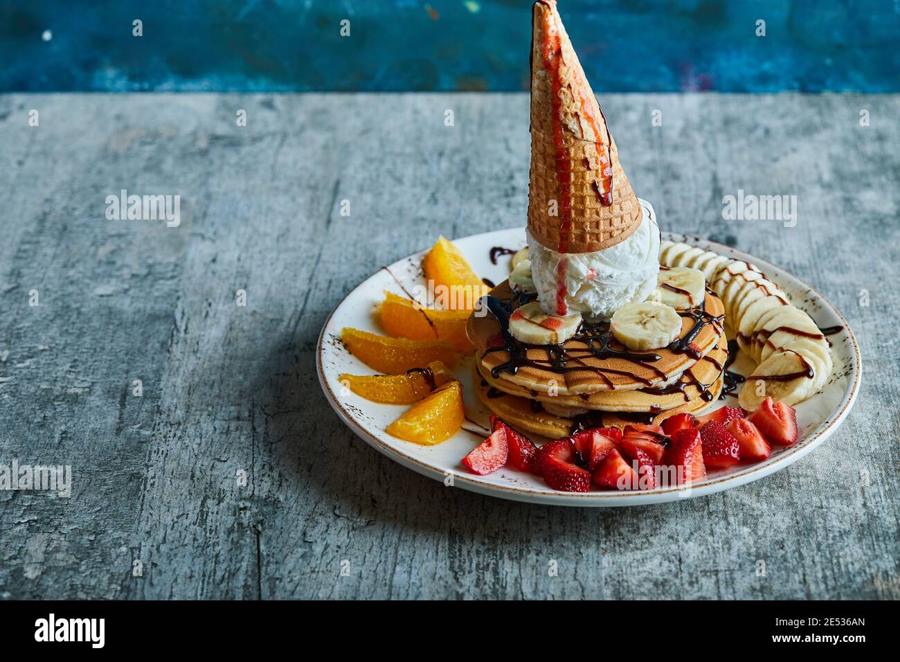 Pfannkuchen mit Eiskegel, Mandarine, Erdbeere, Banane und Schokoladensirup in der weißen Platte auf dem Marmorboden Stockfoto