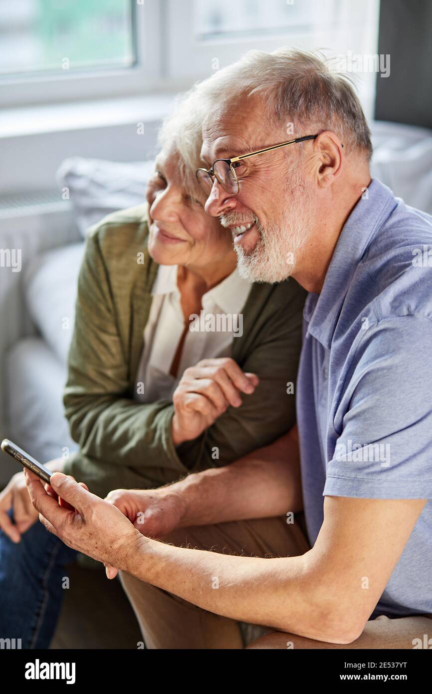 Ältere kaukasische Paar zu Hause mit Smartphone, sie sitzen zusammen, Ruhe, lächelnd Stockfoto