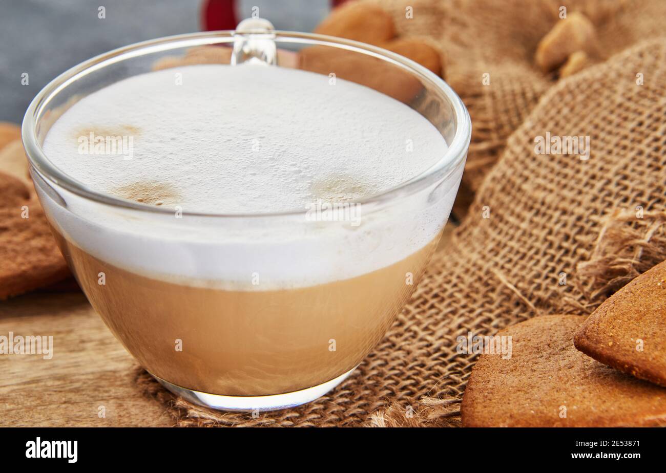 Eine Tasse Cappuccino-Kaffee und Lebkuchen in der Form eines Herzens auf einem Sackleinen Hintergrund Stockfoto