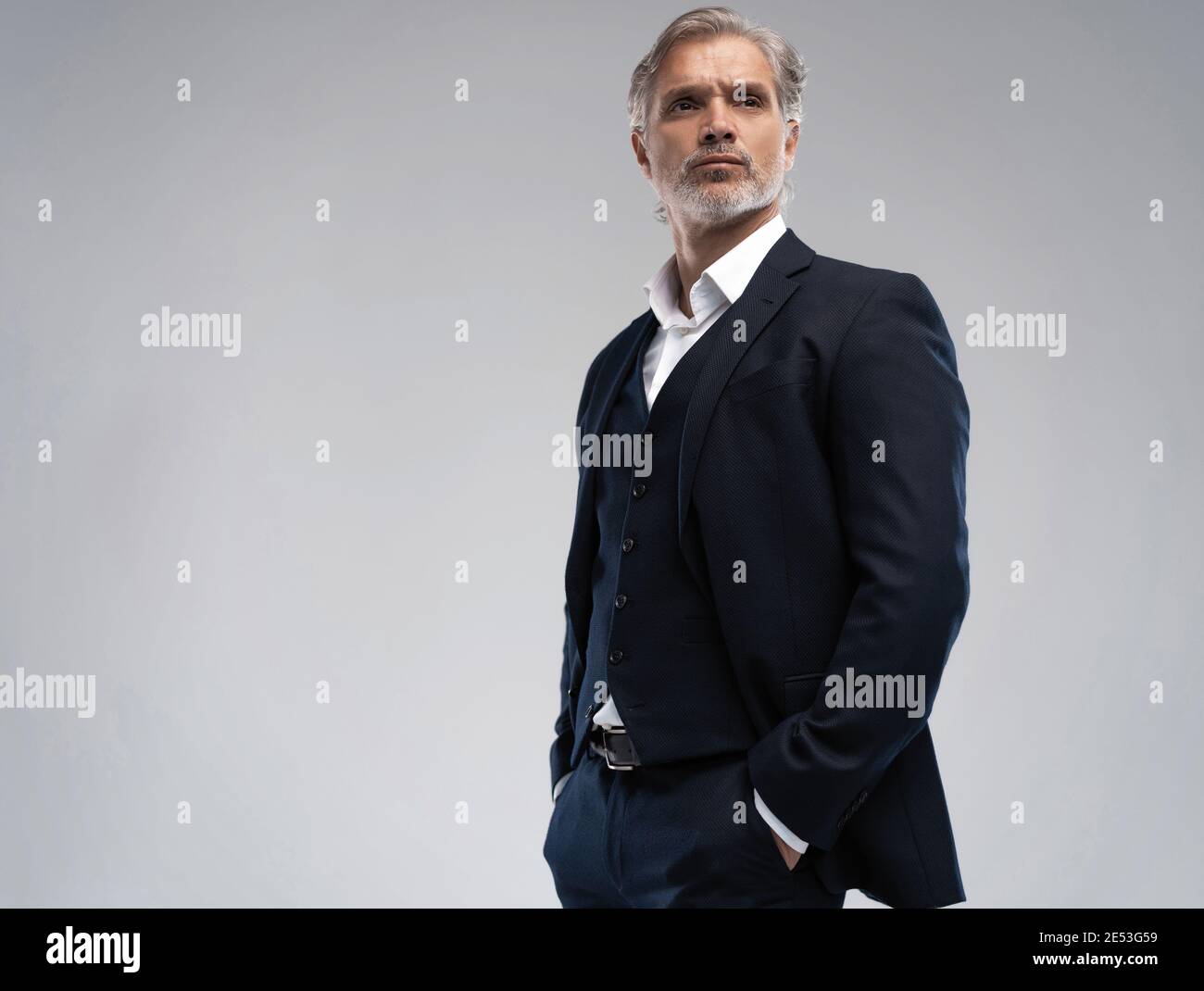 Schöner Mann mittleren Alters in Anzug posiert vor grauem Hintergrund Stockfoto
