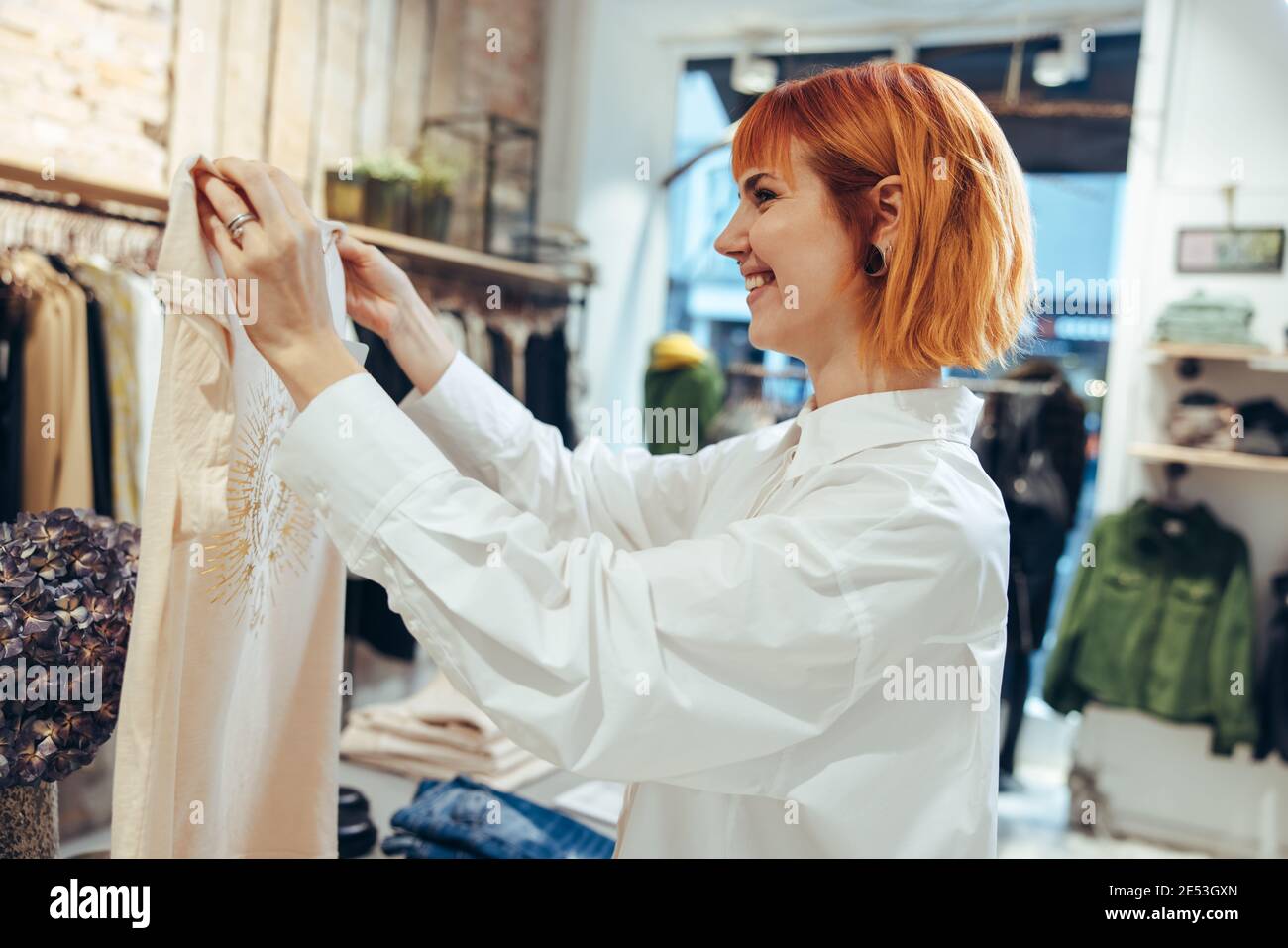 Frau, die ein Hemd hält und dem Kunden im Geschäft zeigt. Inhaber des Modehaus, der den Kunden im Geschäft unterstützt. Stockfoto