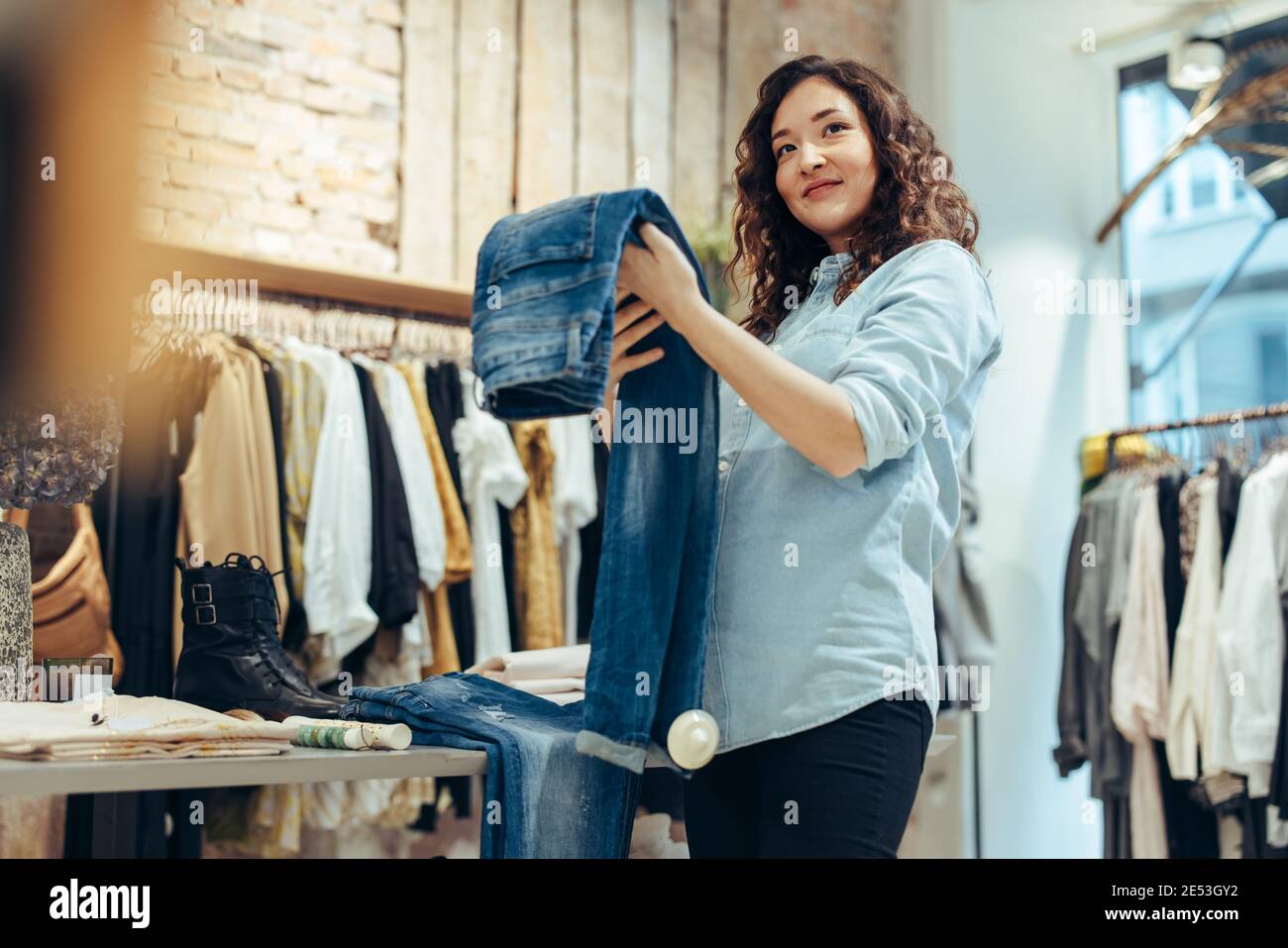 Frau hält Jeans und schaut weg, während sie im Geschäft einkaufen. Frauen einkaufen im Bekleidungsgeschäft. Stockfoto