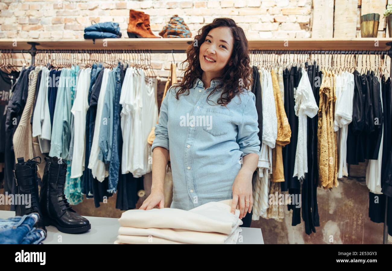 Weibliche Einkäufe in einer Boutique. Frau, die in die Kamera schaut und beim Einkaufen in einem Bekleidungsgeschäft lächelt. Stockfoto