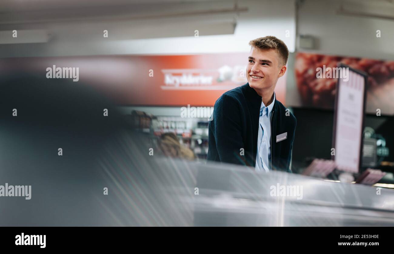 Junger männlicher Arbeiter, der in einem Supermarkt arbeitet. Mann auf einem Ferienjob im Lebensmittelgeschäft. Stockfoto