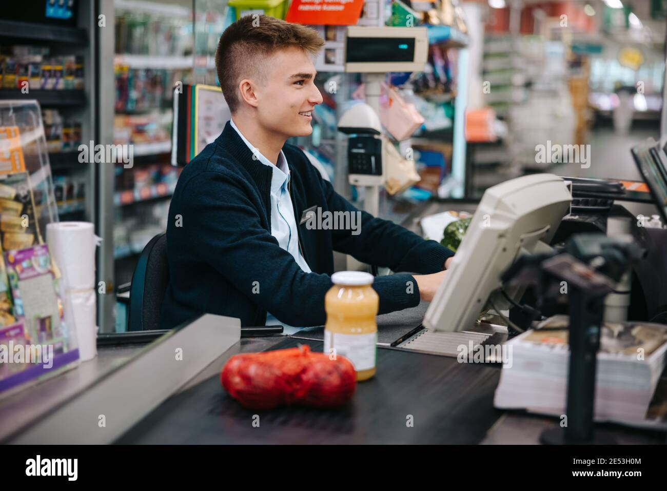Mann, der an der Kasse des Lebensmittelladens arbeitete. Junger Arbeiter im Supermarkt im Urlaub. Stockfoto