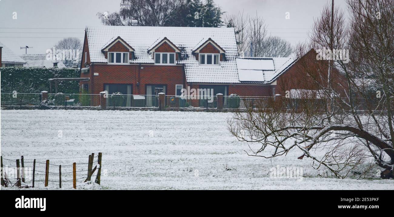 Eine Winterpostkartenszene mit einem schönen roten Backsteinhaus Und angrenzendes Feld in einer Decke von Schnee bedeckt Stockfoto