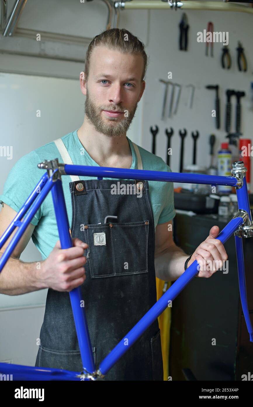 Ein junger und stilvoller Mann mit Jeanschürze repariert ein Fahrrad in einem Geschäft. Geschäftsinhaber bei der Arbeit Stockfoto