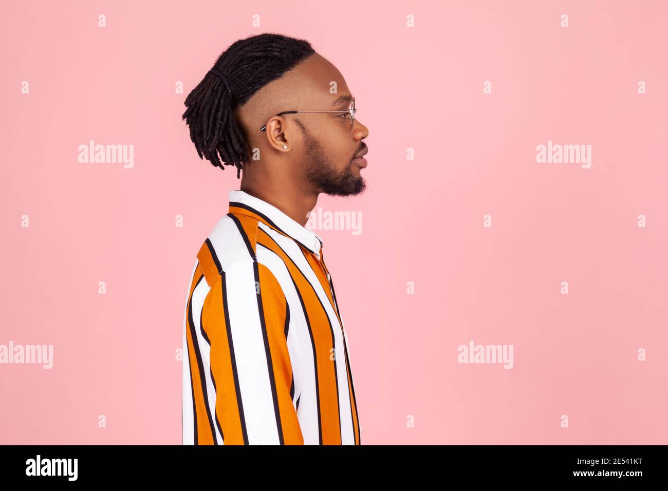 Profilportrait stilvoller afro-amerikanischer Mann mit Dreadlocks und Ohrpiercing im gestreiften Hemd ernsthaft nach vorne schauen, Zukunft planen. Studio im Innenbereich Stockfoto