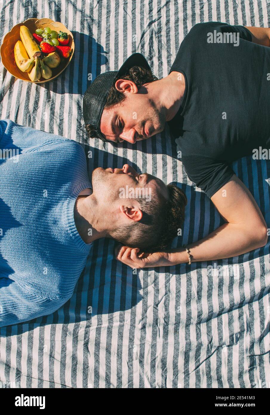 Zarte Gay paar Blick auf einander liegen auf Striped Tischdecke Picknick mit Obstkorb Stockfoto