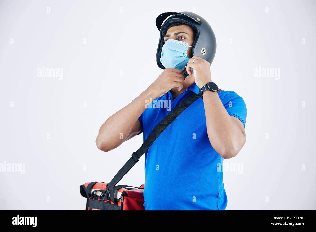 Develiry Mann in medizinische Maske mit Kühltasche auf seinem Schulter auf Helm setzen Stockfoto