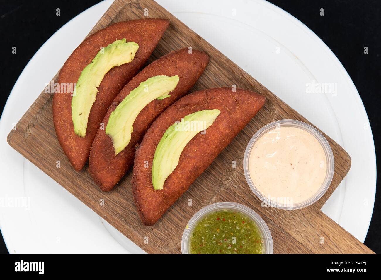 Blick von oben auf die kulinarischen mexikanischen Speisen Lieblings-Gebäck Empanadas serviert auf einem Holzschneidbrett und gekrönt mit in Scheiben geschnittenen Avocado. Stockfoto