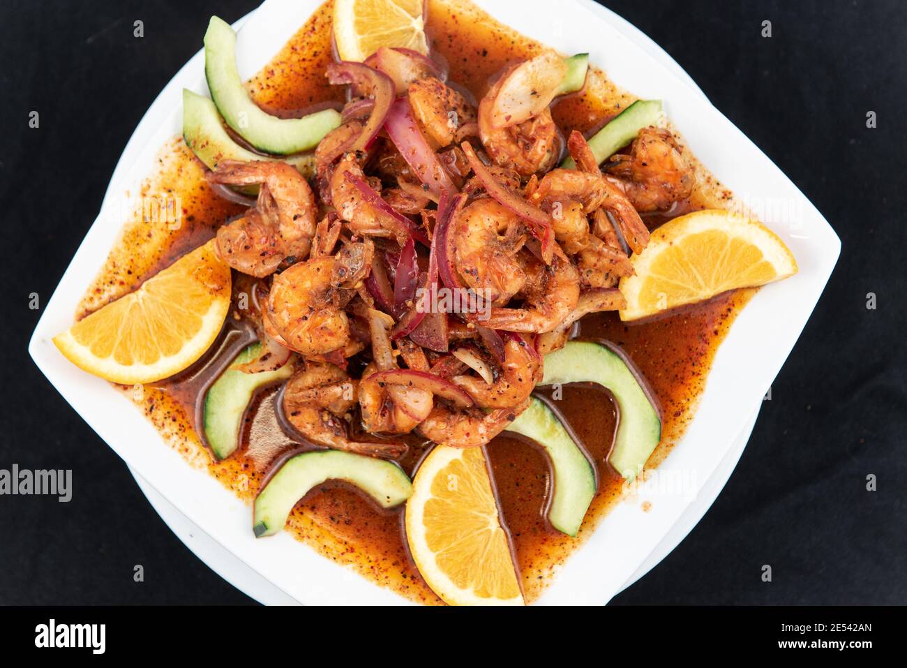Blick von oben auf einen würzigen Teller mit Garnelen mit mexikanischem Geschmack Mit Orangenscheiben und Gurke Stockfoto