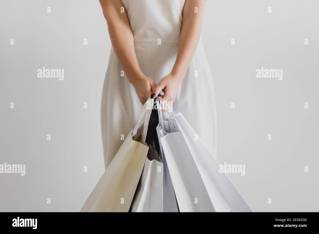 Cropped Ansicht der Frau in weißem Kleid hält Einkaufstaschen auf weißem Hintergrund. Stockfoto