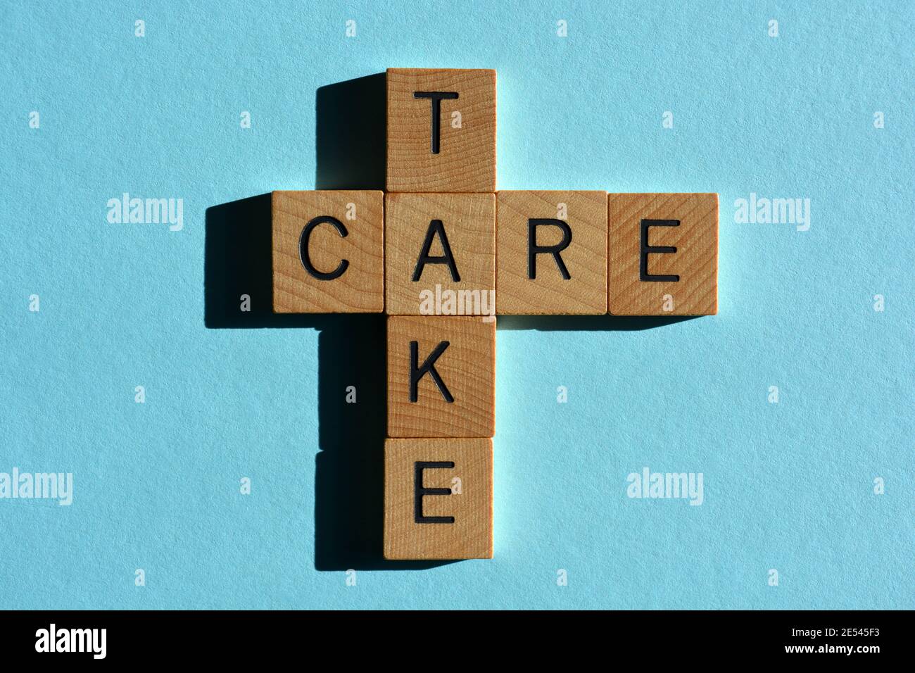Take Care, Wörter in Holz-Alphabet Buchstaben in Kreuzworträtsel-Form isoliert auf blauem Hintergrund Stockfoto