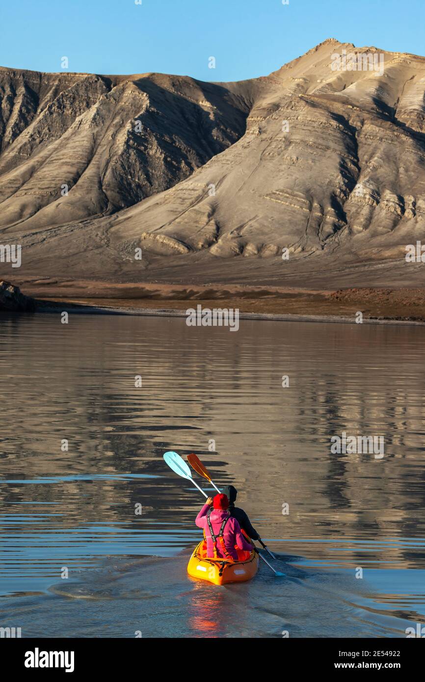 Eine Person in einem orangefarbenen Kajak paddelt in Richtung Berge in Baffin Bay Stockfoto