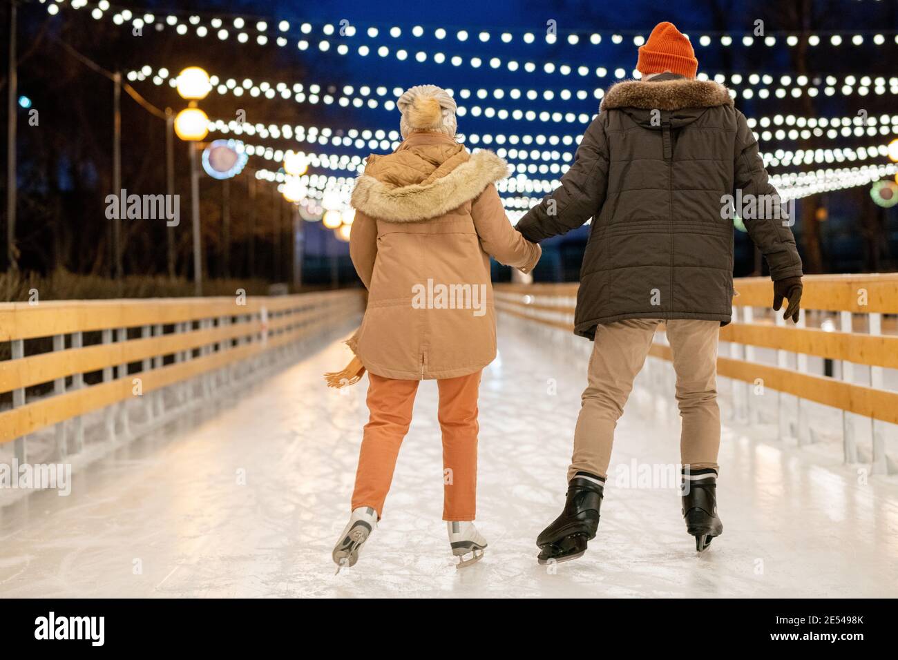 Rückansicht des Paares, das die Hände hält und das Skaten lernt Gemeinsam auf der Eisbahn im Freien Stockfoto