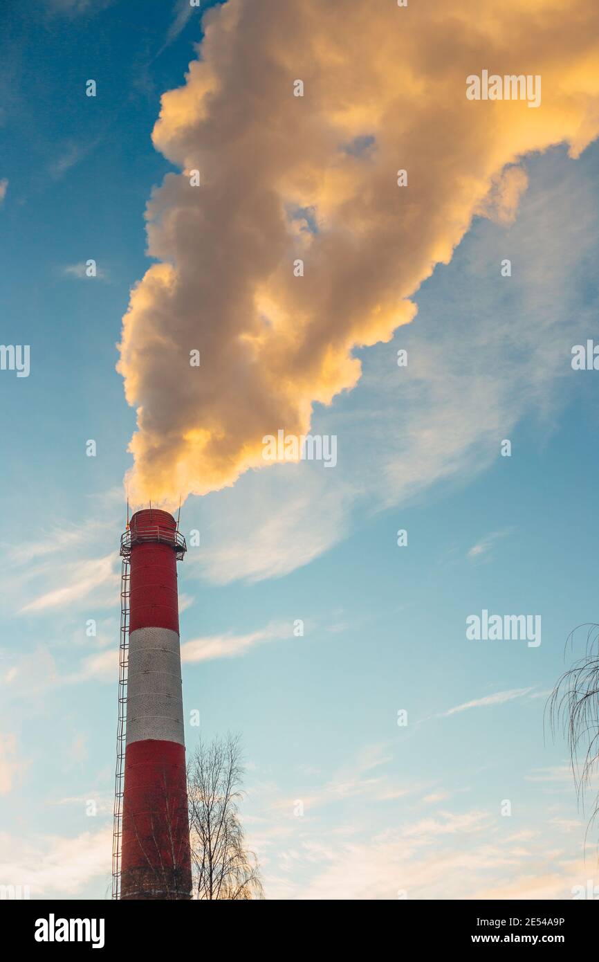 Der hohe Schornstein des Kesselraums im Frost gegen die Himmel mit gelbem Rauch - Heizperiode Stockfoto