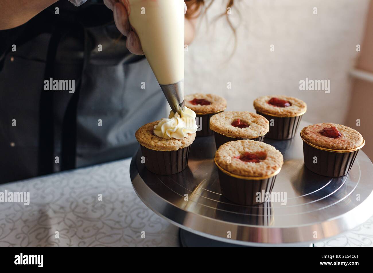 Das Mädchen kocht Cupcakes zu Hause. Hände eines Küchenchefs mit einer Tüte, die Sahne auf die Cupcakes quetschen Stockfoto