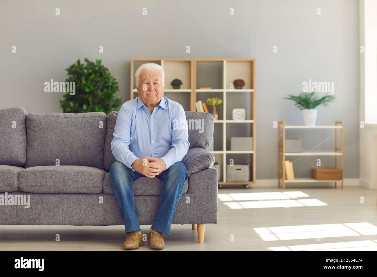 Weißhaariger älterer Mann, der allein auf der Couch zu Hause sitzt und Über sein Leben nachzudenken Stockfoto