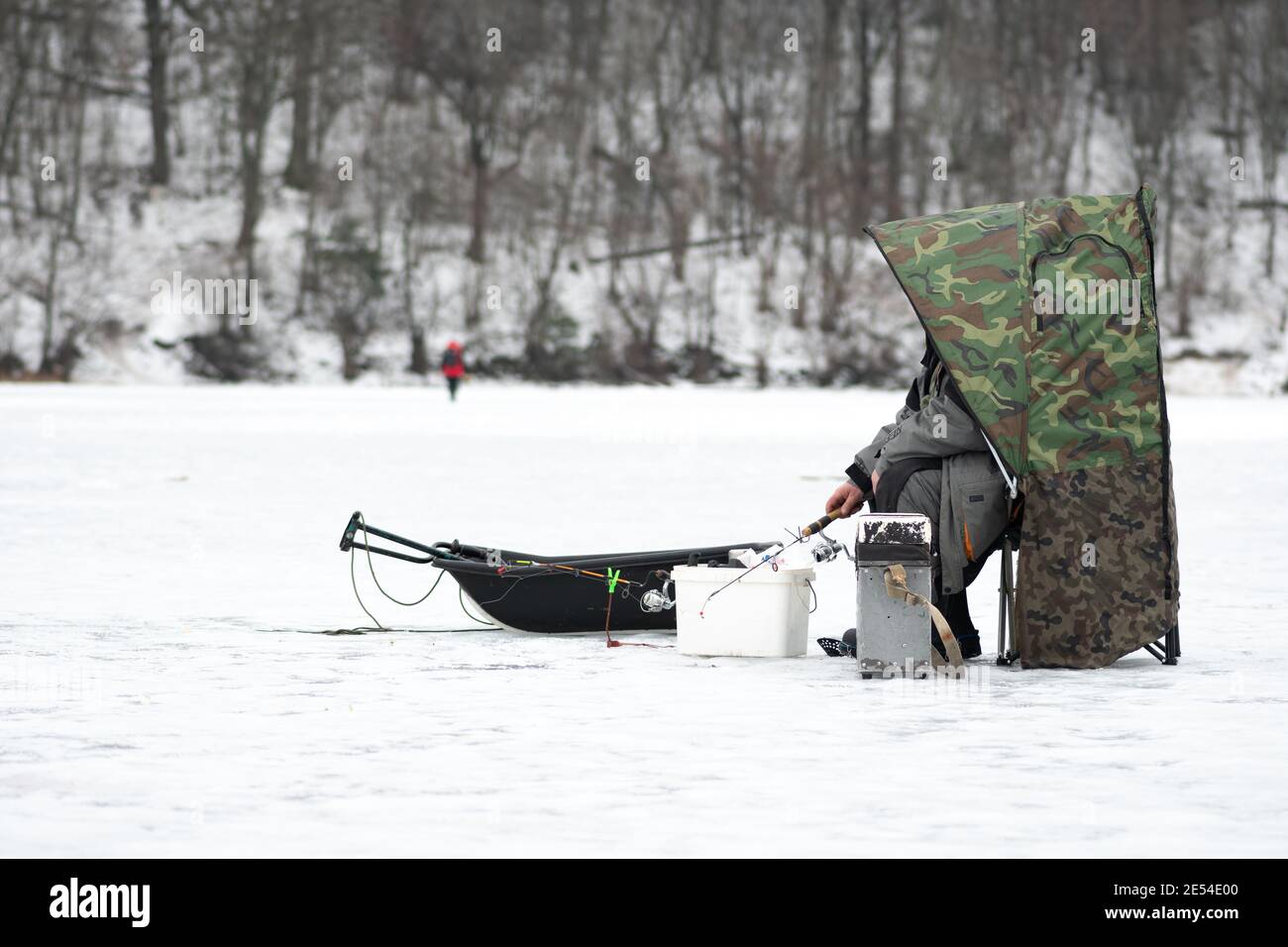 Fischer Angeln auf einem gefrorenen See im Winter mit Zelt, Angelrute oder Rute, Eisschnecke und Ausrüstung zum Angeln Stockfoto