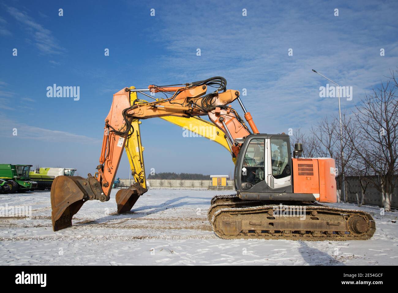 Orange und gelb kraftvolle Raupenbagger stehen auf einer Baustelle. Miete, Leasing für Erdarbeiten. Schnee, Winter, sonnig Stockfoto