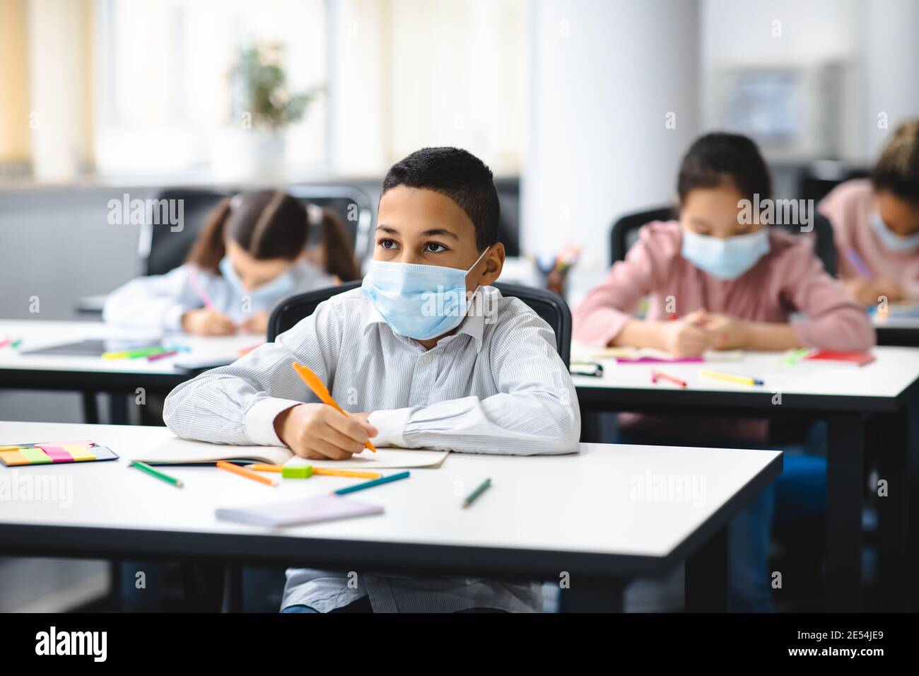 Junge in Maske sitzt am Schreibtisch im Klassenzimmer Stockfoto