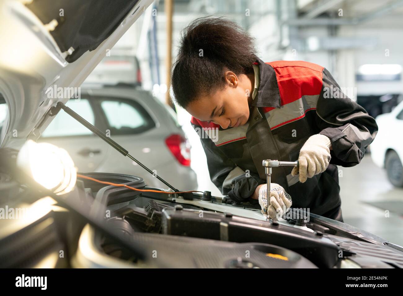 Professioneller Techniker der Kfz-Wartung, der durch offenen Motor steht Fach in der Werkstatt und mit Handwerkzeug, um kleine Details zu fixieren Stockfoto