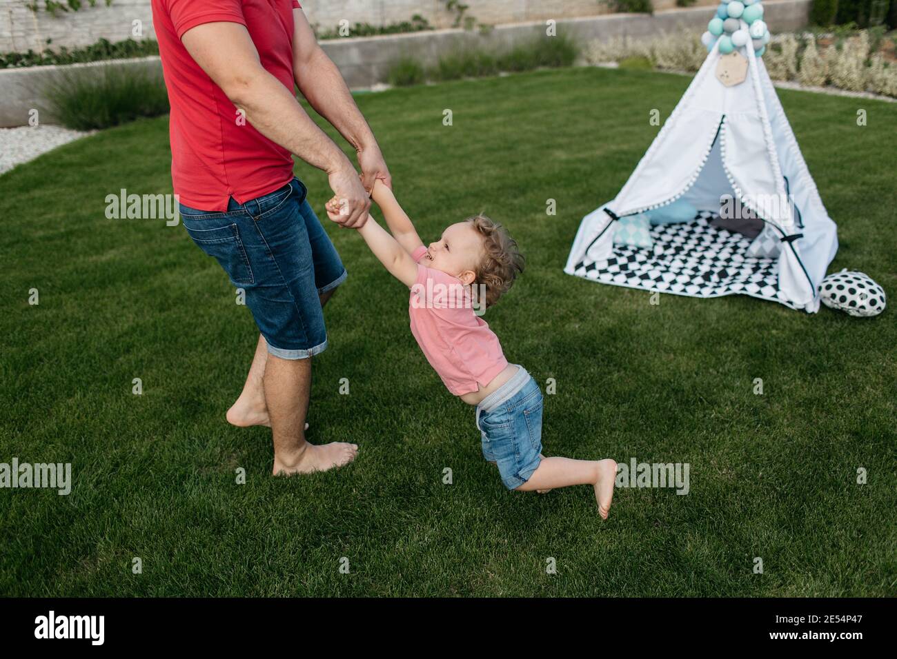 Vater dreht seinen kleinen Sohn draußen im Garten. Glückliches Kind, das Spaß mit seinem Vater hat. Stockfoto