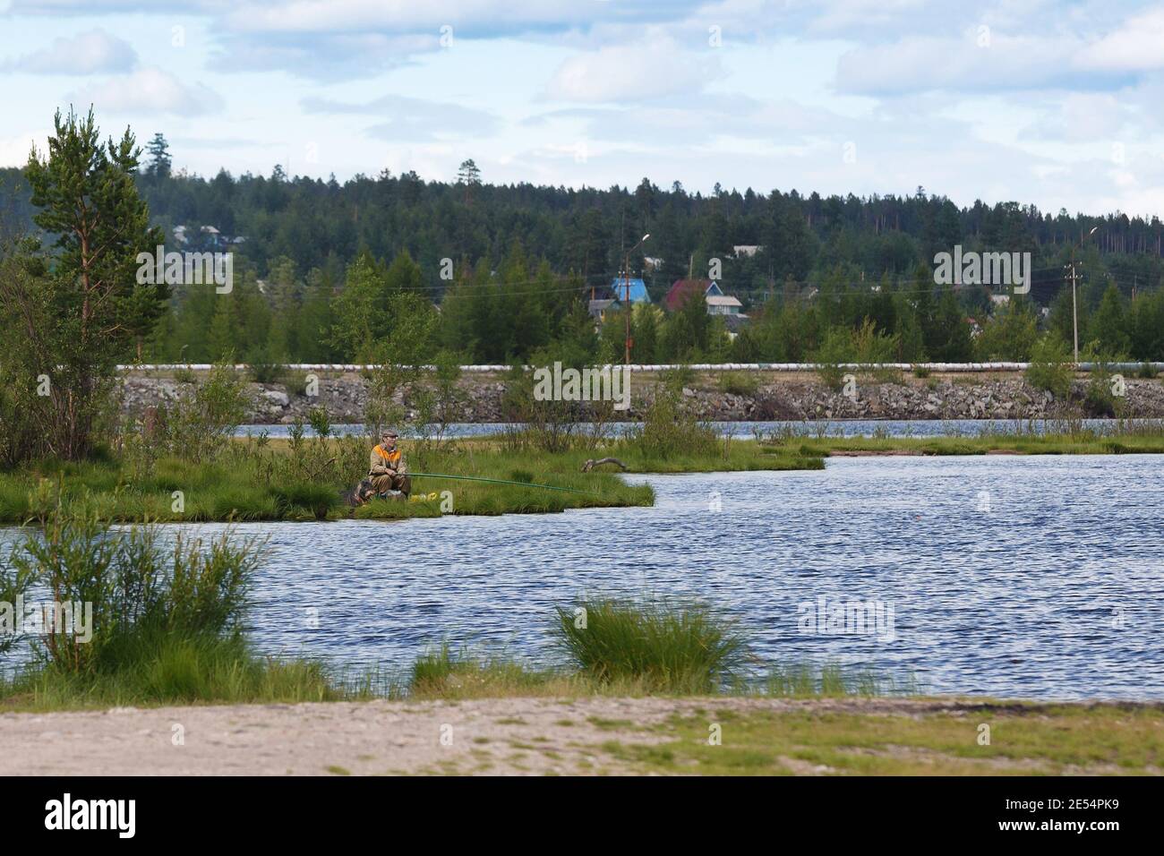 Bezirk Neryungri, Jakutien, Russland. 13. Juli 2016 EIN Mann fischt in einem Teich vor dem Hintergrund eines Waldes und Häuser. Stockfoto