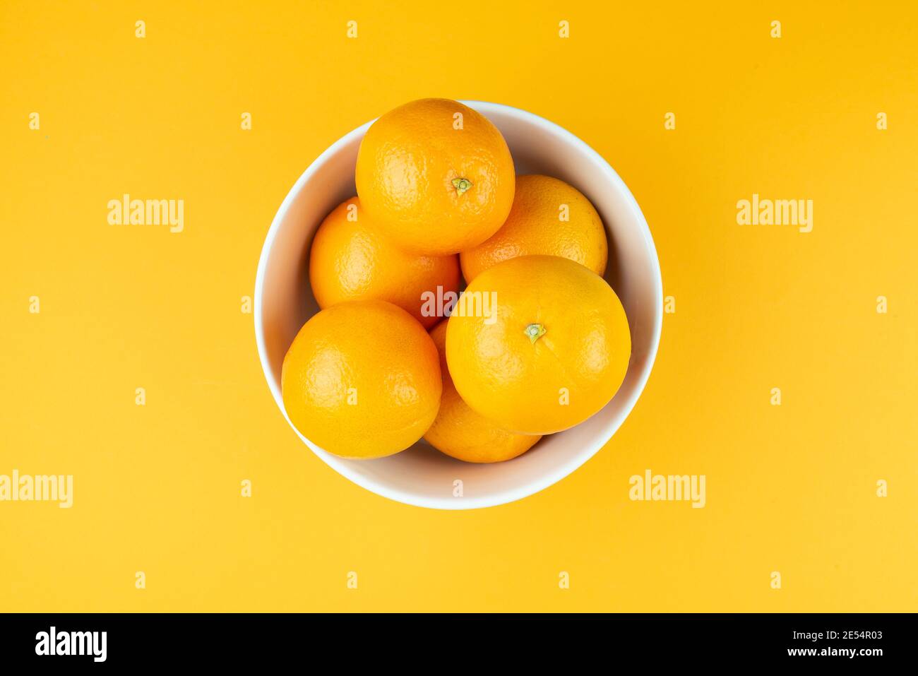 Direkt über der Ansicht der weißen Schüssel mit saftigen Orangen gefüllt Auf orangefarbenem Hintergrund Stockfoto