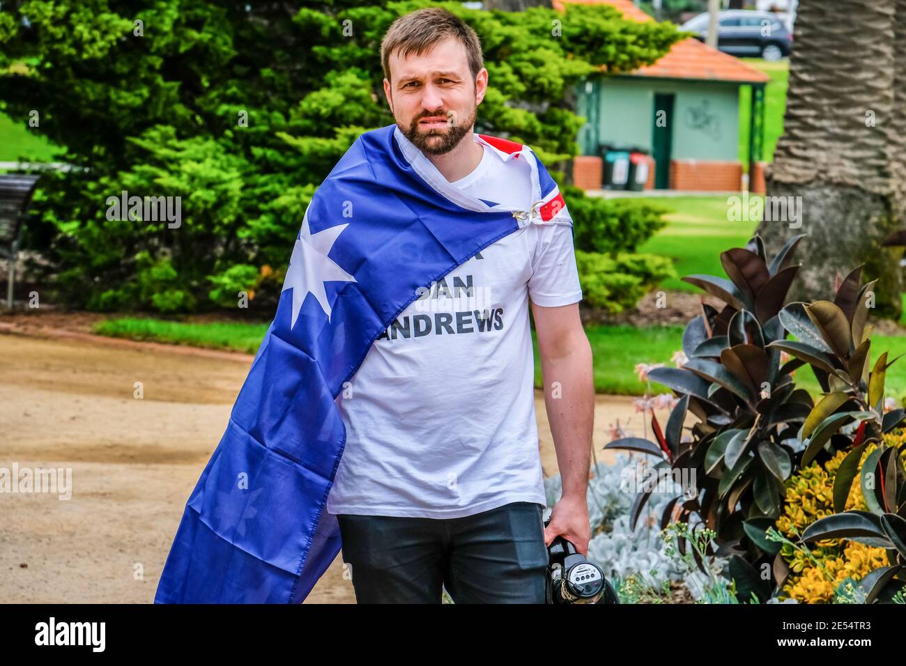 Melbourne, Australien. Januar 2021. A1-Aktivist wird während der Feierlichkeiten zum Australia Day in die australische Flagge gehüllt mit dem T-Shirt „Lack Dan Andrews“ gesehen. Mitglieder der Partei „extreme Right Australia One“ (A1) veranstalteten eine friedliche Demonstration und Feier zu Ehren des Australia Day, der jährlich am 26. Januar in den Catani Gardens in St. Kilda begangen wird. Kredit: SOPA Images Limited/Alamy Live Nachrichten Stockfoto