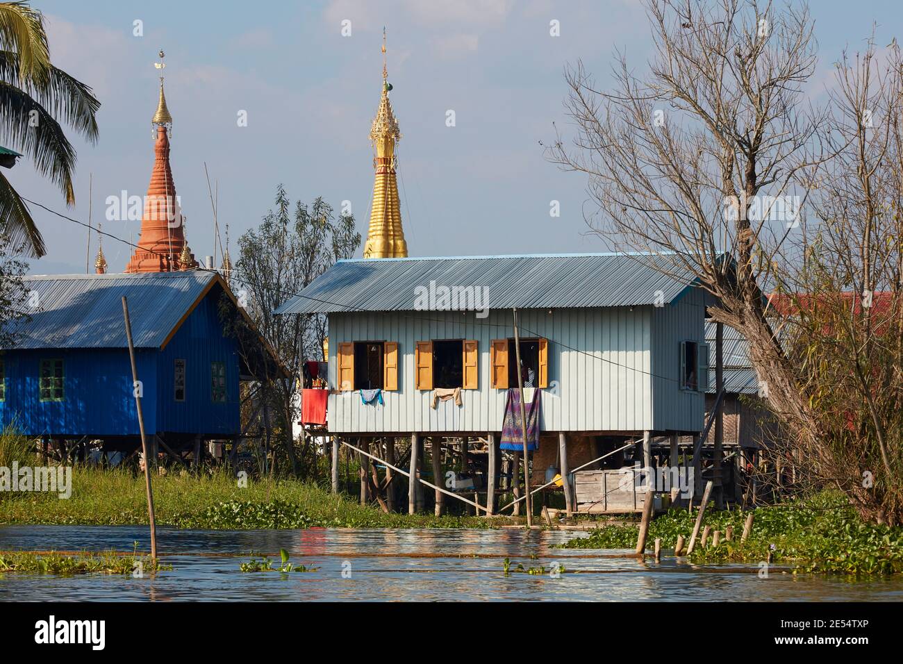 Ein traditionelles Inle Lake Stelzenhaus mit buddhistischen Stupas im Hintergrund, Myanmar. Stockfoto