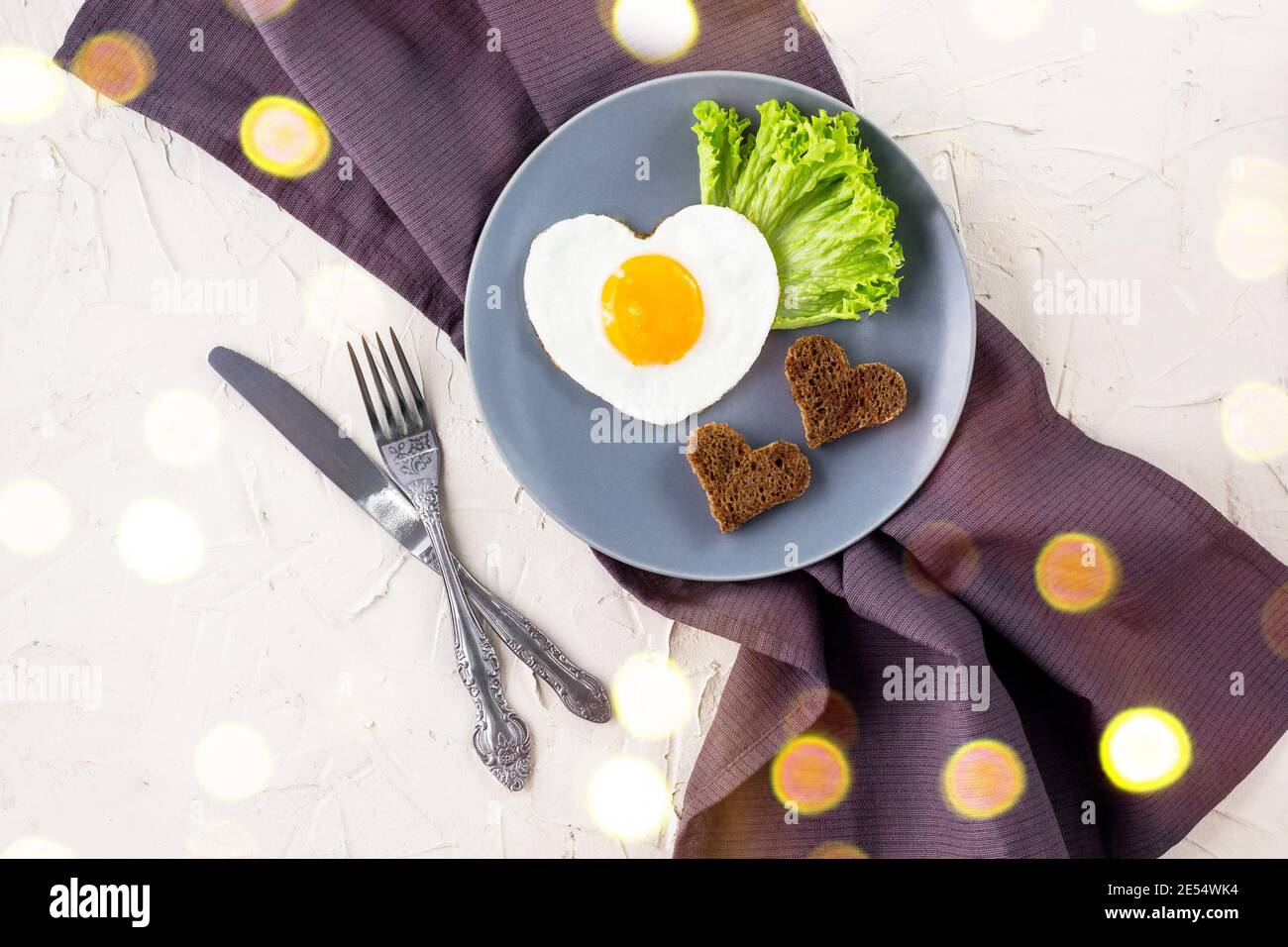 Valentinstag Frühstück mit herzförmigen Spiegelei serviert auf grauen Teller. Flach legen, Blick von oben mit Bokeh Stockfoto