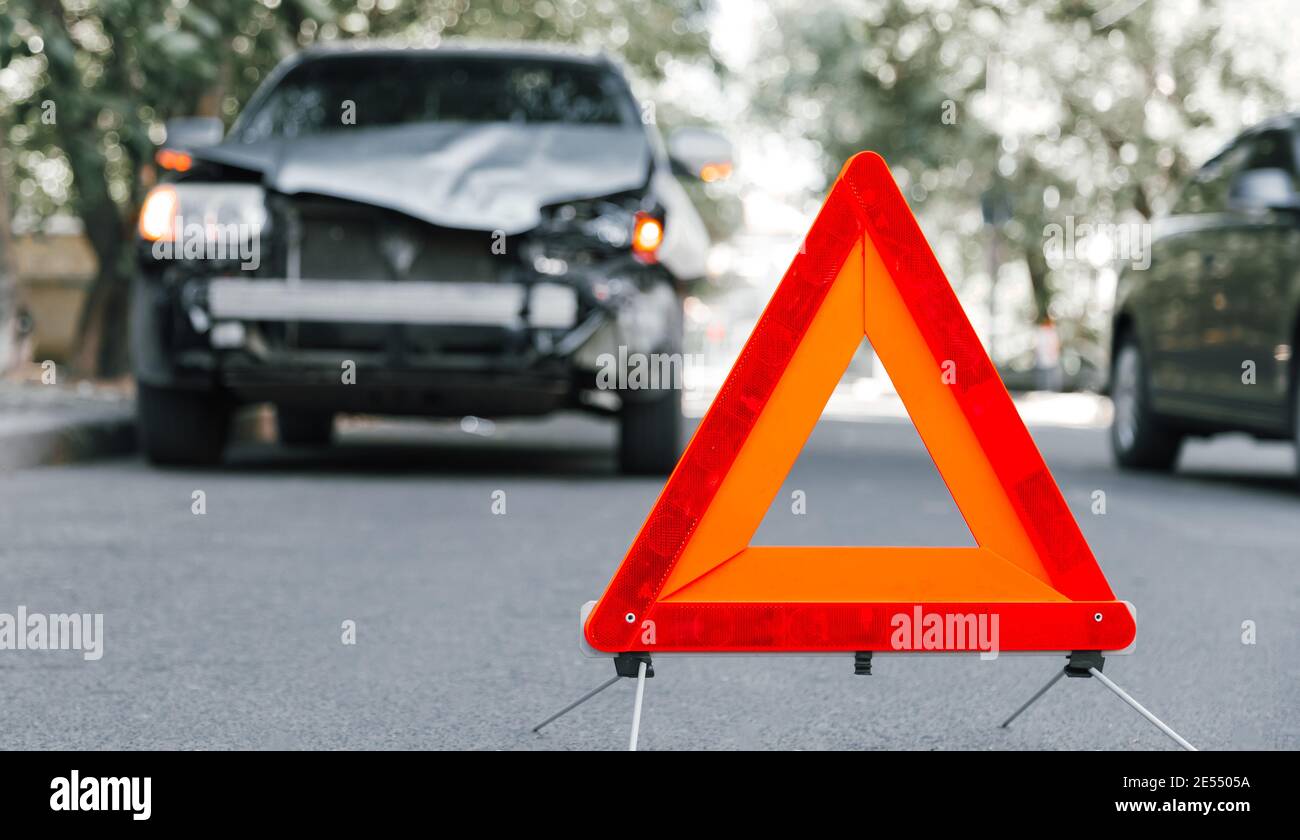 Rote Not-aus-Dreieck-Schild auf der Straße in Autounfall Szene. Gebrochenes SUV-Auto auf der Straße bei Verkehrsunfall. Autounfall Verkehrsunfall auf der Stadtstraße Stockfoto