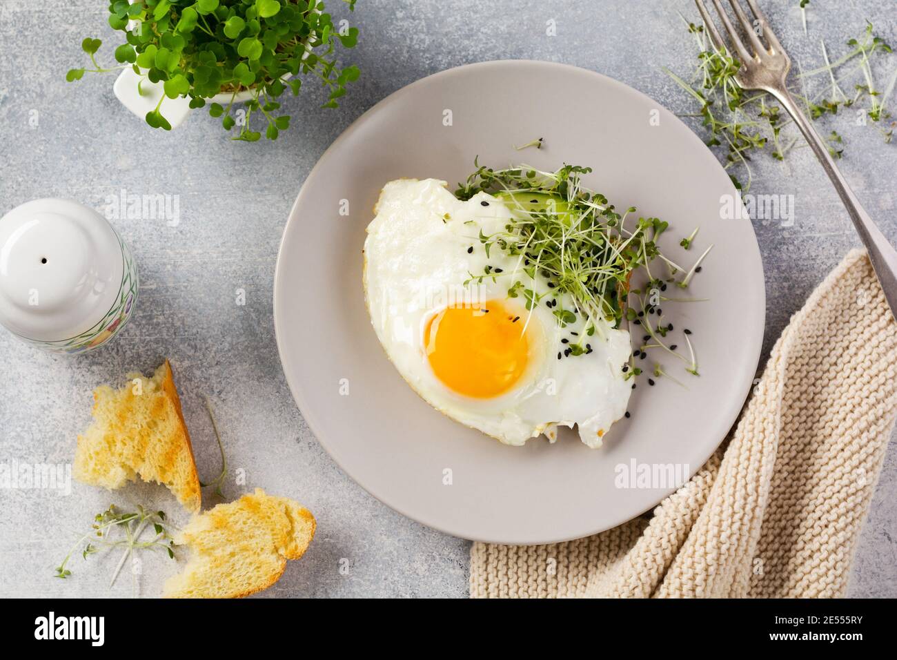 Traditionelles englisches Frühstück mit Spiegeleiern mit Rucola microgreen in grauer Keramikplatte auf grauem Beton altem Hintergrund. Draufsicht. Stockfoto