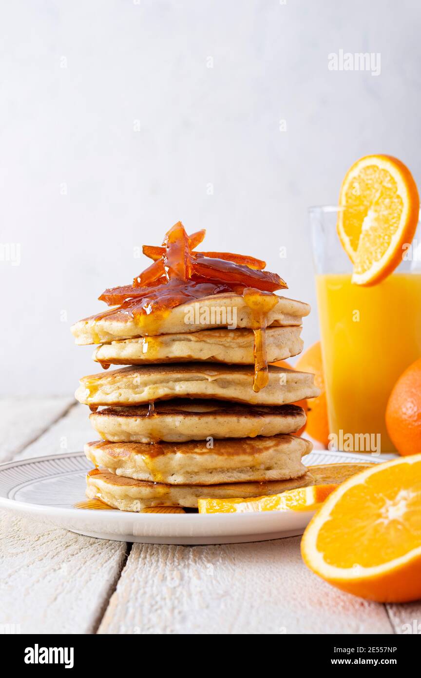 Pfannkuchenturm mit Orangenmarmelade, frischen Orangen und Saft zum Frühstück auf rustikalem Holztisch Stockfoto