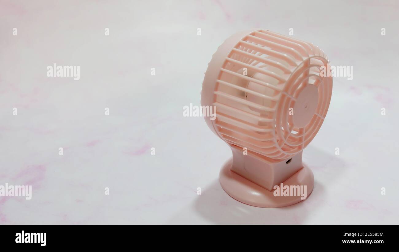 Ein kleiner tragbarer pinker Ventilator, auf einer rosa marmorähnlichen Oberfläche. Stockfoto