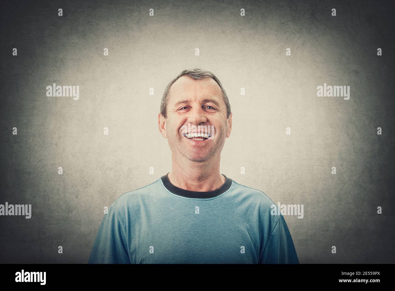 Glücklicher Mann mittleren Alters lächelnd trägt lässige T-Shirt isoliert über grauen Wand Hintergrund. Porträt des fröhlichen männlichen Senior lacht überglücklich, positiv Stockfoto