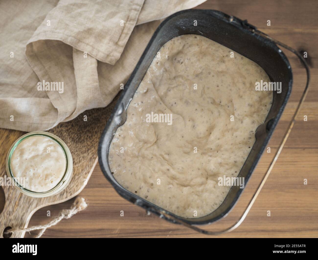 Weizensauerteig Starter im Glasgefäß und Sauerteig in der Brotpfanne der Brotmaschine. Hausgemachtes Brotbackkonzept Stockfoto