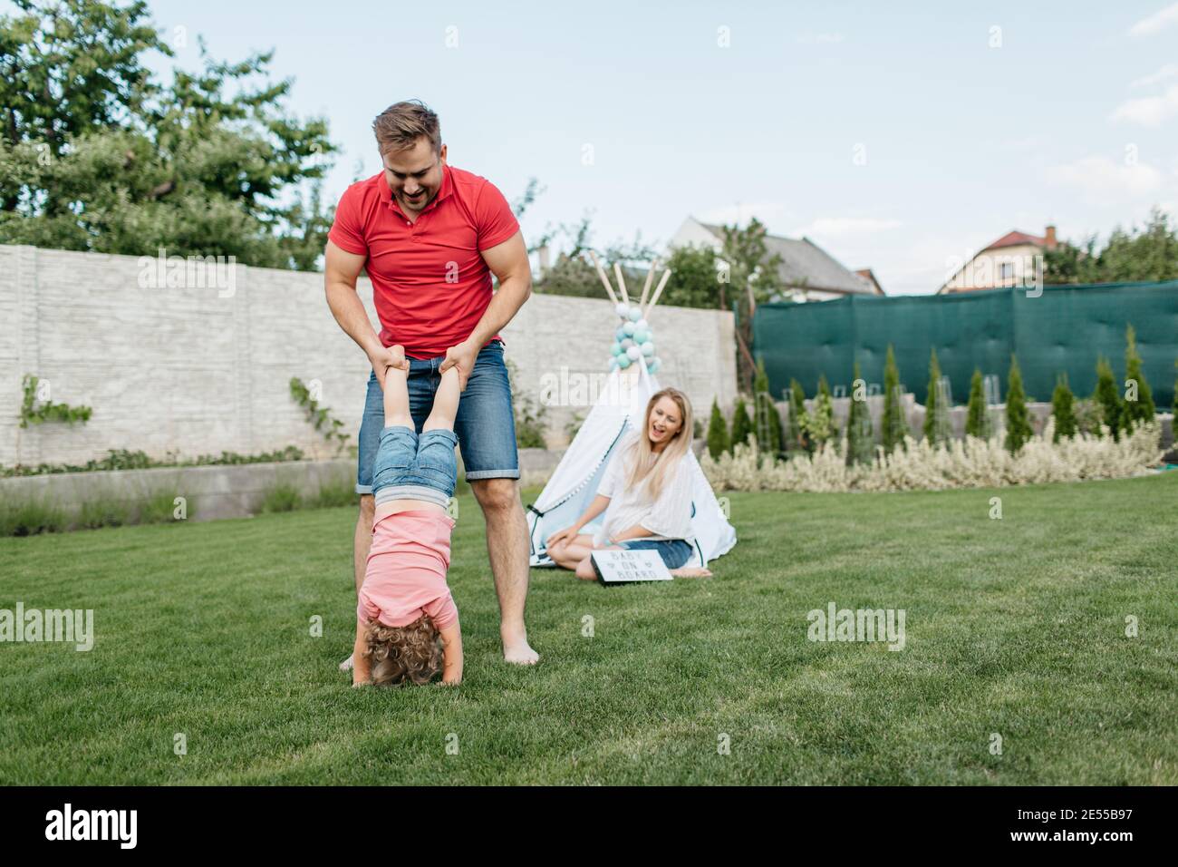 Glückliche Familie verbringen Zeit zusammen draußen im Garten. Kind, das Spaß mit seinen Eltern hat und mit einem Vater auf dem Rasen spielt. Stockfoto