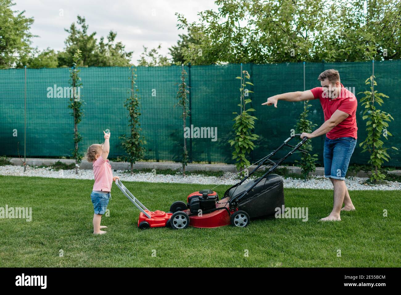 Vater und sein Sohn haben Spaß beim Mähen des Rasens zusammen. Die ganze Länge eines glücklichen Jungen Schneiden das Gras mit seinem Vater. Stockfoto