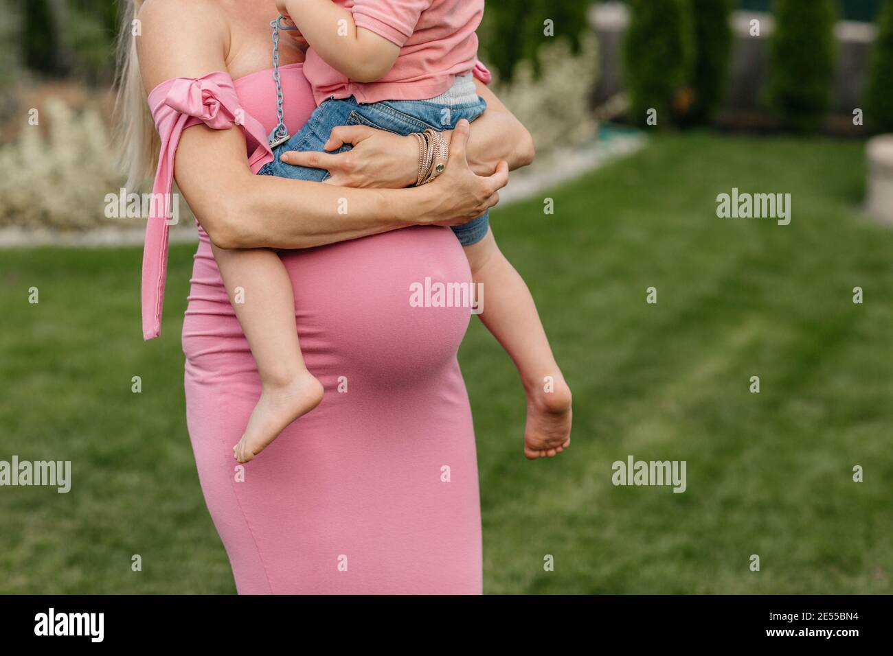 Zugeschnittenes Bild einer schwangeren Frau, die ihr älteres Kind kuschelt. Werdende Mutter hält ihren Sohn in den Armen und ruht ihn auf seiner Schwangerschaft Beule. Stockfoto