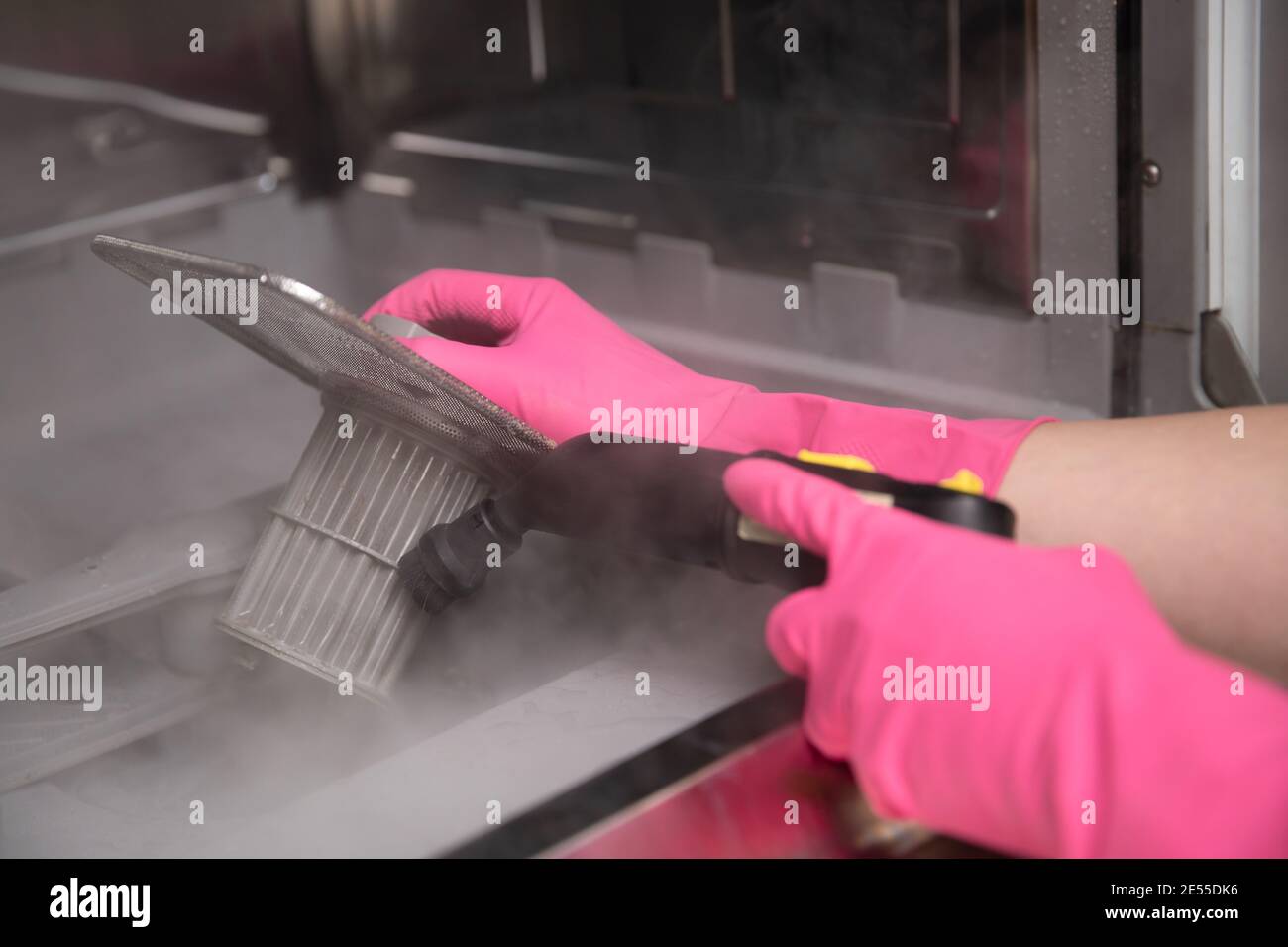 Hausfrau in Gummihandschuhen Reinigung Geschirrspüler Filter mit einem heißen Dampfreiniger. Frühjahrsputz. Stockfoto
